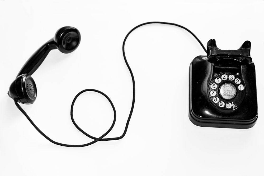 Foto eines schwarzen Wählscheibentelefons vor weißem Hintergrund