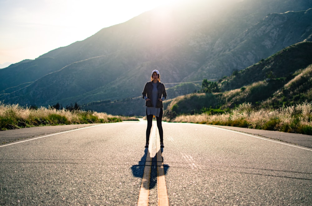 Fotografía de la vista del ojo del gusano de la mujer parada en medio del camino rodeada de árboles y montaña