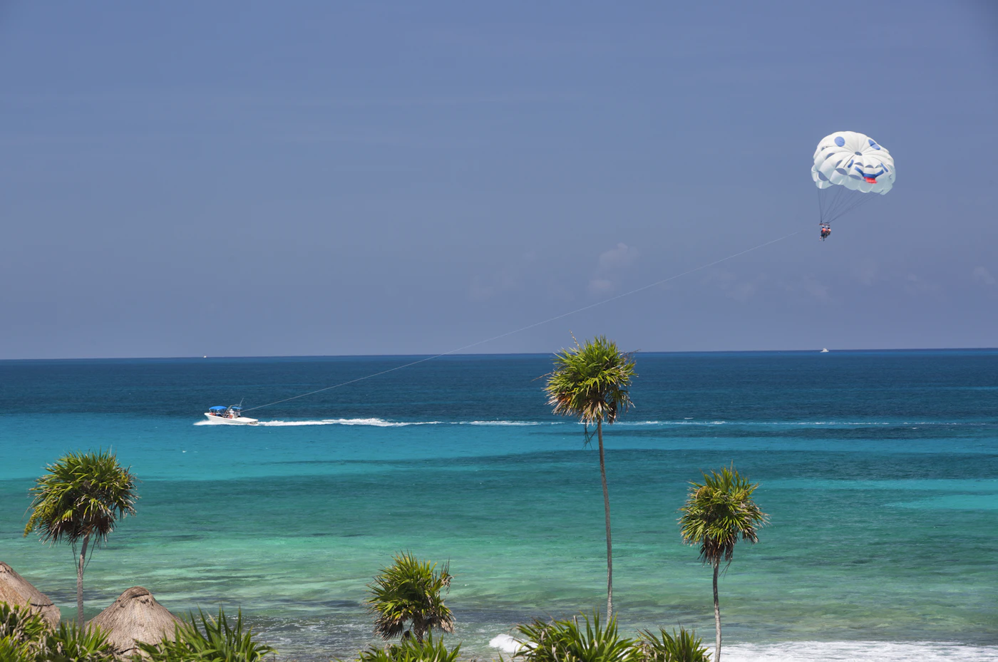 Mar turquesa y palmeras en Playa del Carmen, con un parasail en el cielo