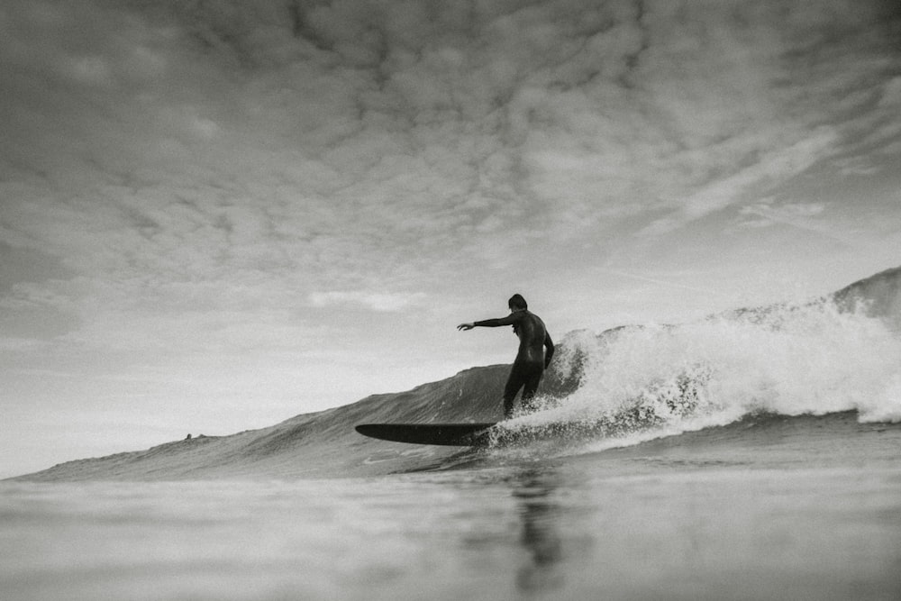 grayscale photo of person surfing under cloudy sky
