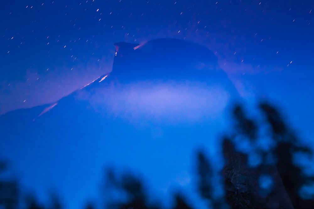 Un cielo notturno con una montagna e alberi in primo piano