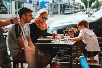 Families enjoying a sunny day sitting at outdoor tables near the mall's food court.