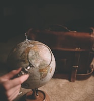 person holding magnifying glass near desk globe