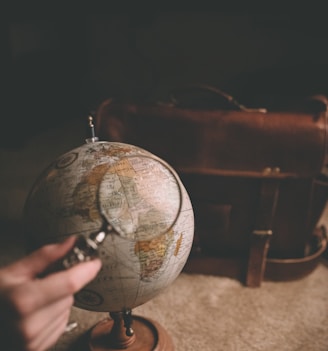 person holding magnifying glass near desk globe