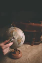 person holding magnifying glass near desk globe