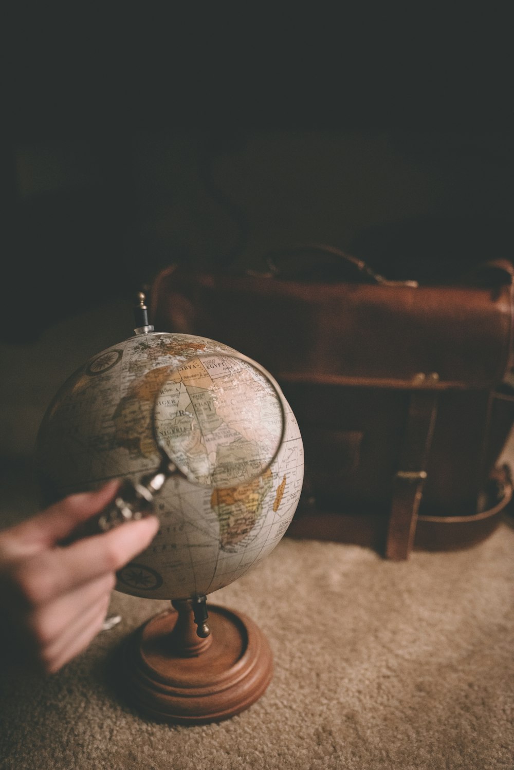 person holding magnifying glass near desk globe