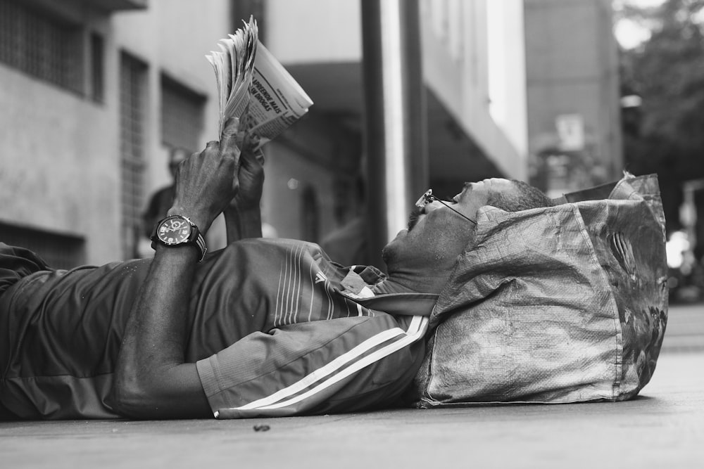 man lying on sidewalk reading newspaper