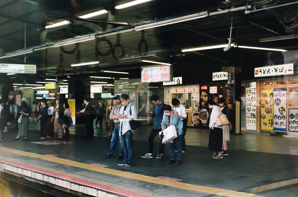people standing near rails while waiting for train