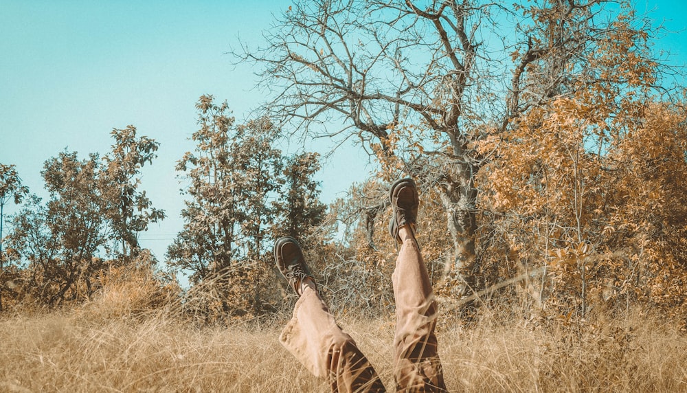 person raises both feet while lying on brown grass