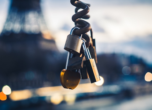 Several metallic locks are attached to a twisted metal wire, with a blurred background of a famous tower and soft bokeh lights.
