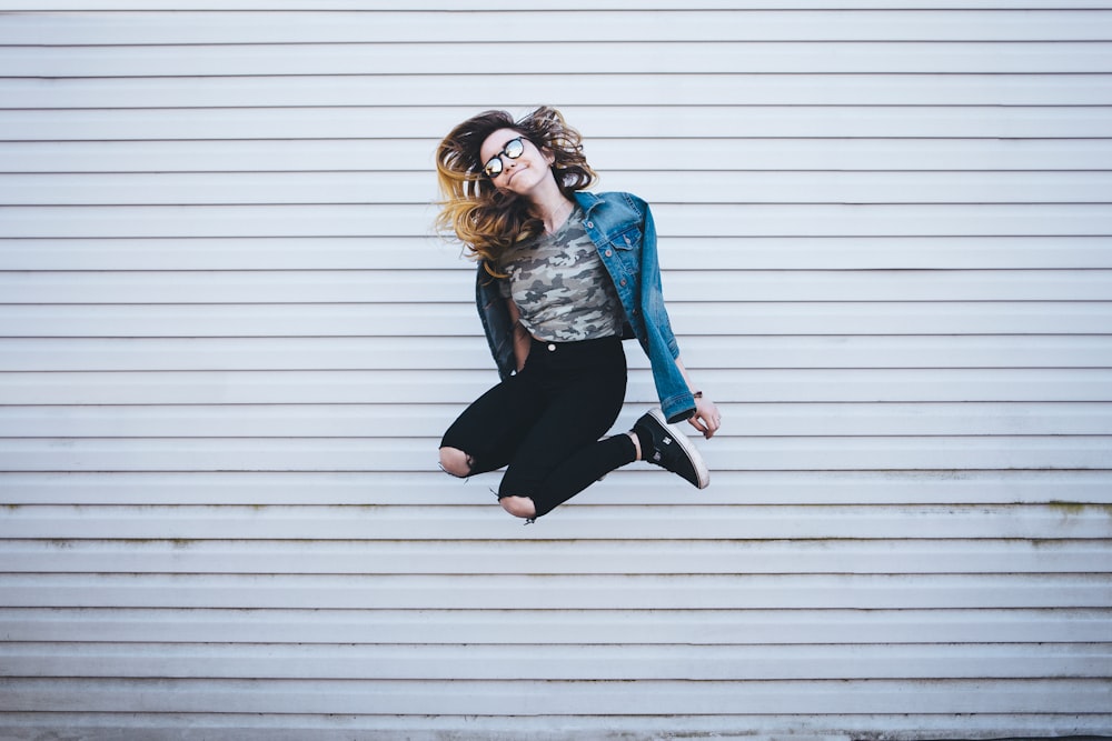 A smiling woman in fashionable casual attire is seen jumping in Toronto.