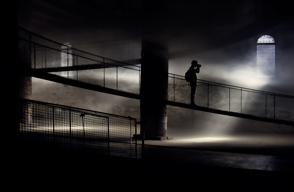 silhouette of person standing on bridge while taking photo