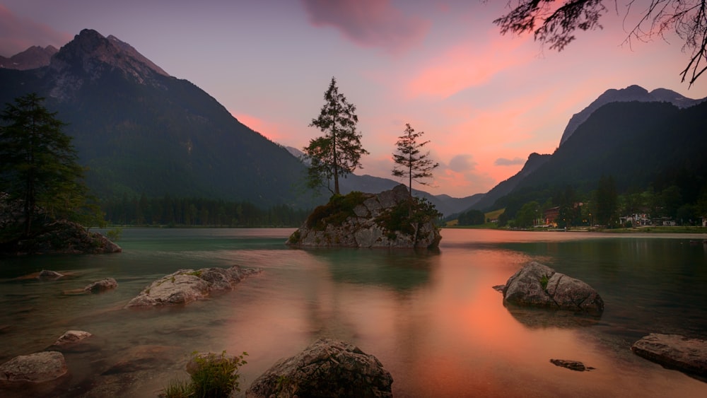 日没時の山の近くの水域に囲まれた岩の上の樹木の風景写真
