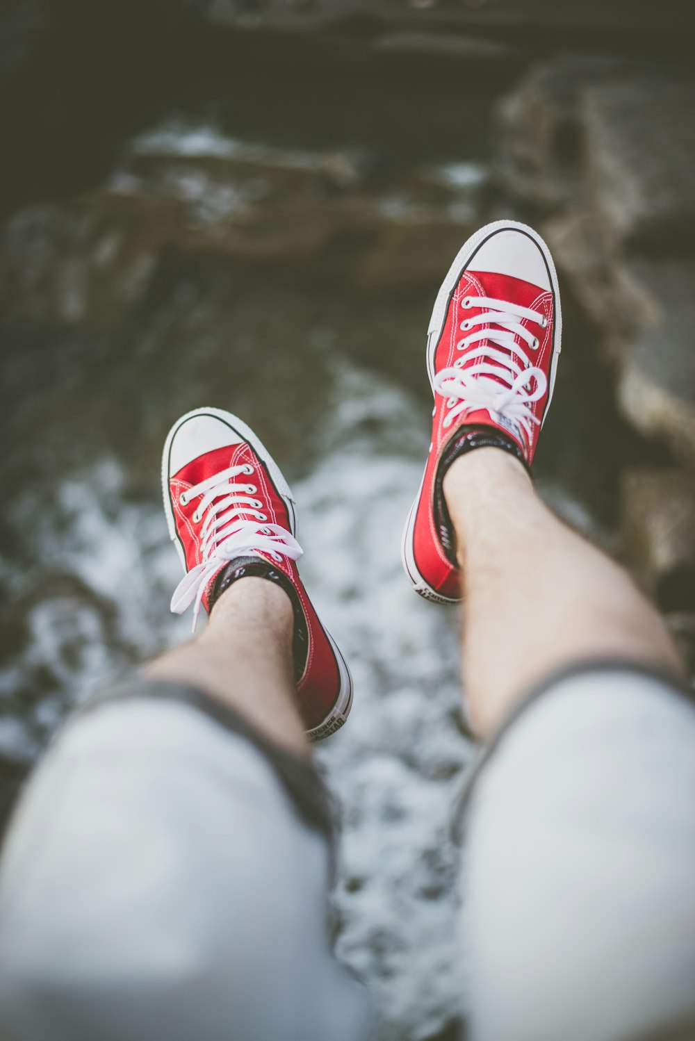 selective focus photography of person wearing red low-top sneakers over body of water