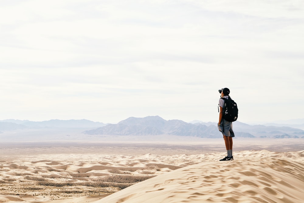 uomo in piedi e zaino portante in terra desertica
