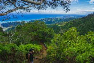 Adventurers hiking a lush volcanic trail with vibrant greenery and distant ocean views.