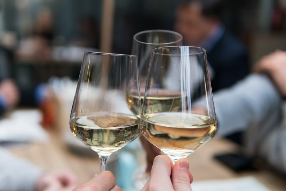 Tres personas brindando con tres copas de vino de cristal transparente