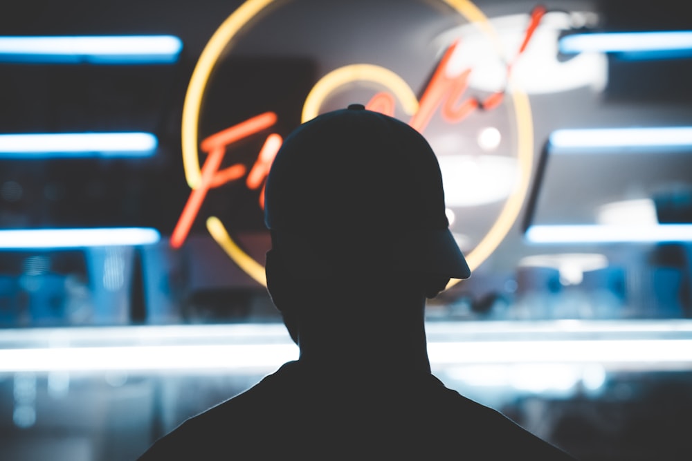 silhouette of man wearing fit cap near LED sign