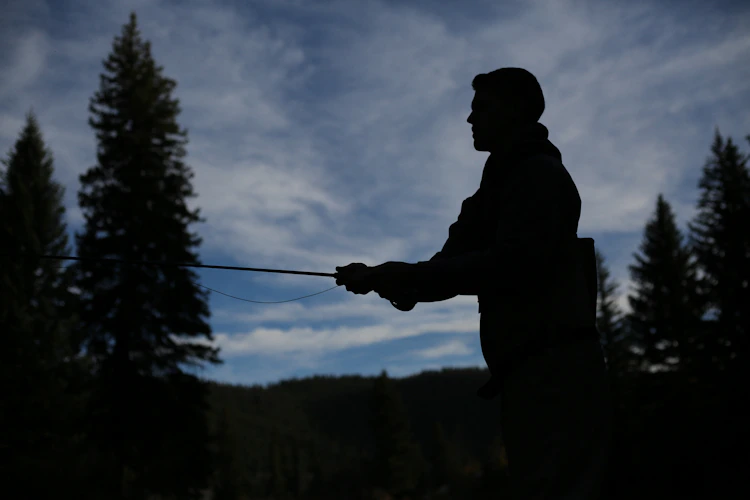 fly fisherman silhouette against blue sky