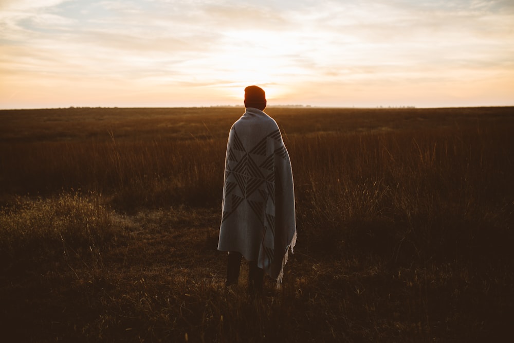 personne couverte d’une robe debout devant un champ d’herbe