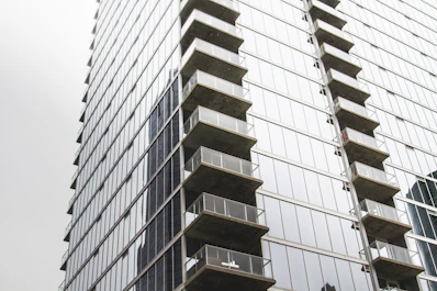 Modern downtown apartment building with glass balconies and city skyline behind.