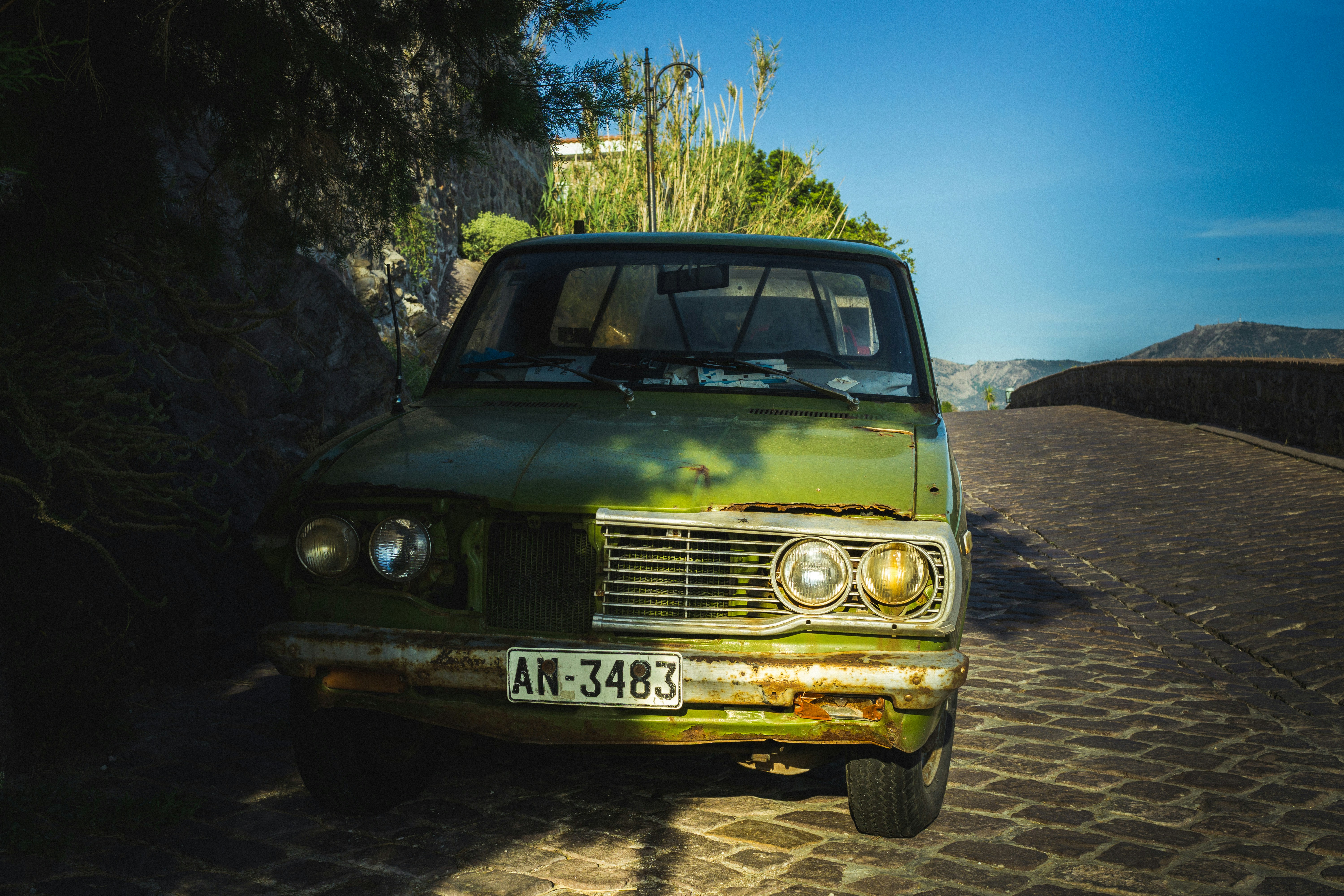 Old rusty car parked on street, overcast sky, weathered paint, urban environment