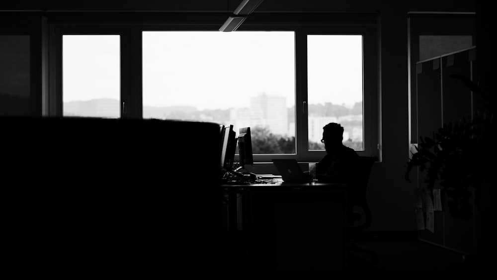 silhouette of man sitting along glass window
