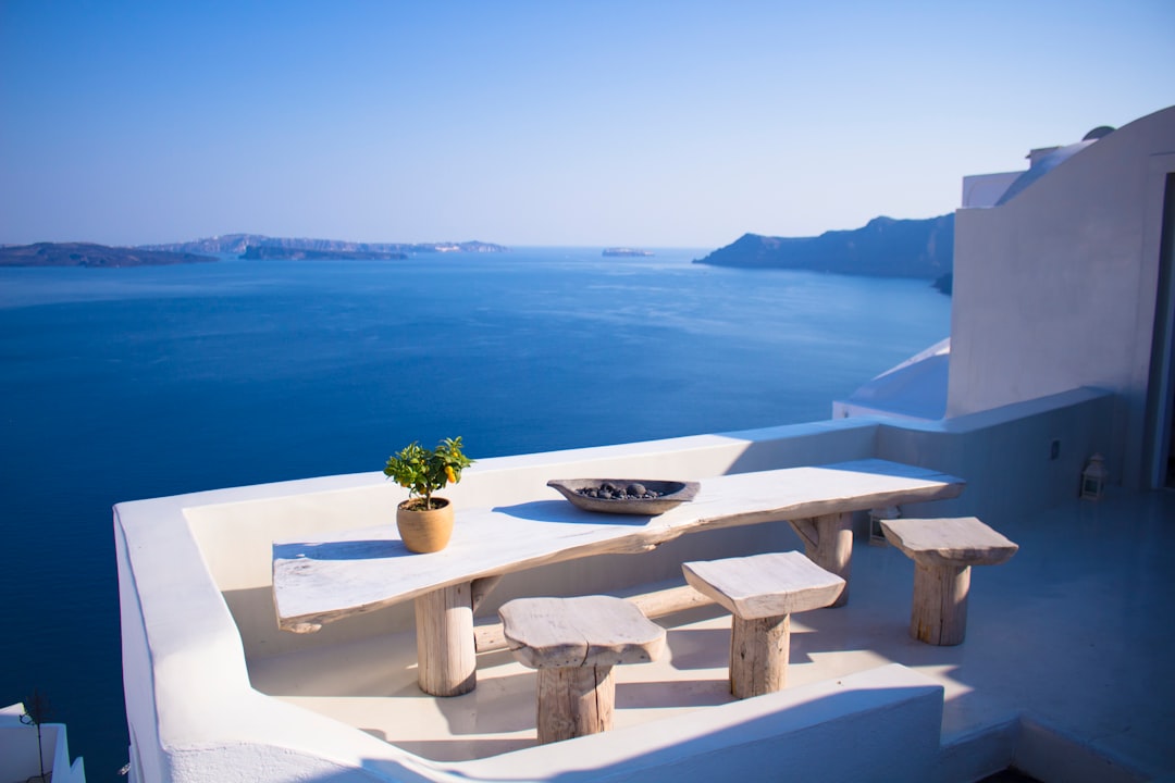 bench and dining table near body of water under calm sky, Very Greek table and view