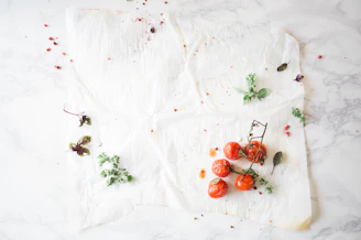 Fresh ripe tomatoes and green herbs laid out on parchment paper, echoing our brand colors.