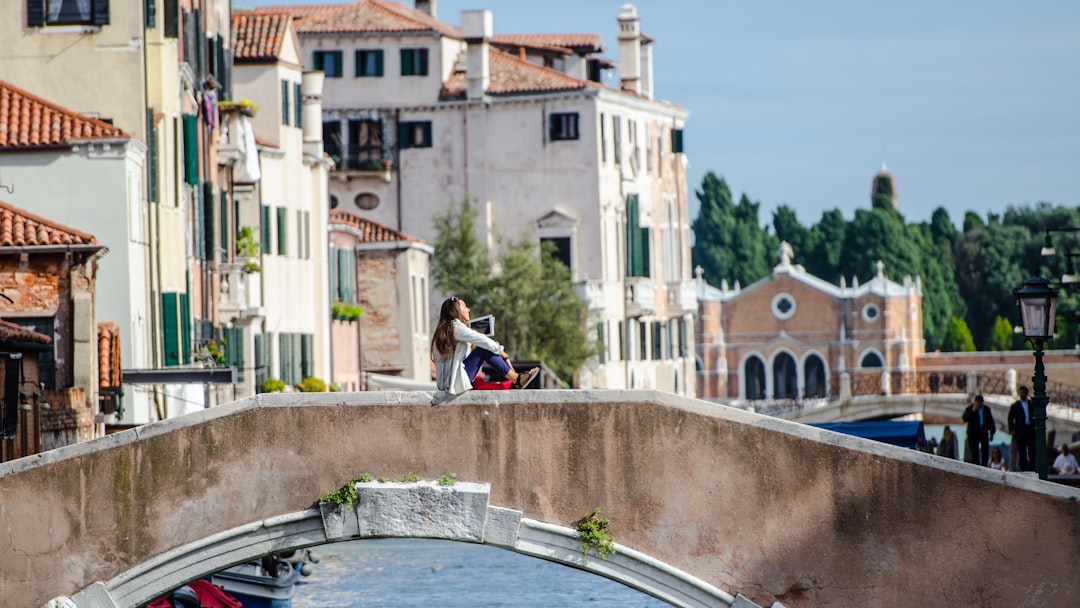 woman sitting on bridge rail over canal,