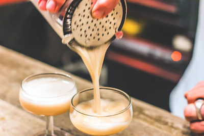 Close-up of a bartender’s hand expertly pouring genever into a chilled coupe glass.