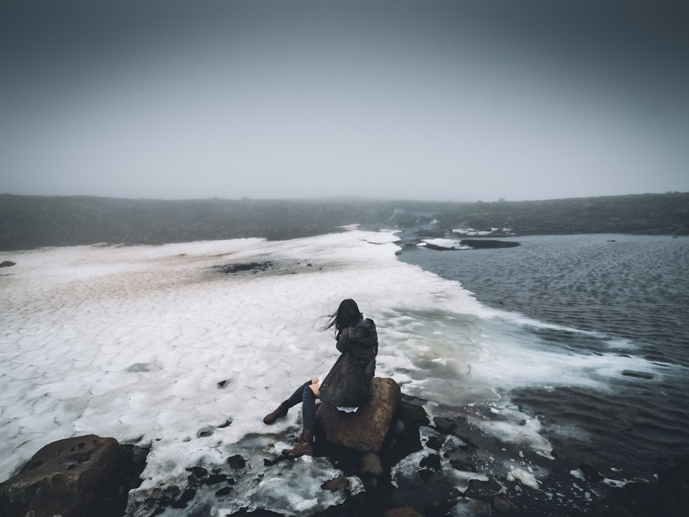 woman sitting on rock near seashore