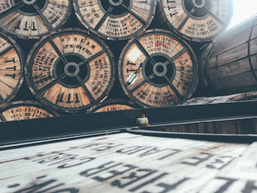 Wooden cable reels are stacked horizontally and vertically, some with visible text and labels. The image has an industrial and vintage feel due to the wear on the wood and muted colors.