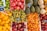 A vibrant display of various fresh fruits neatly arranged in crates. Green apples, pomegranates, pears, melons, oranges, and apricots are stacked in vivid sections. Chalkboard price signs add a rustic market atmosphere.