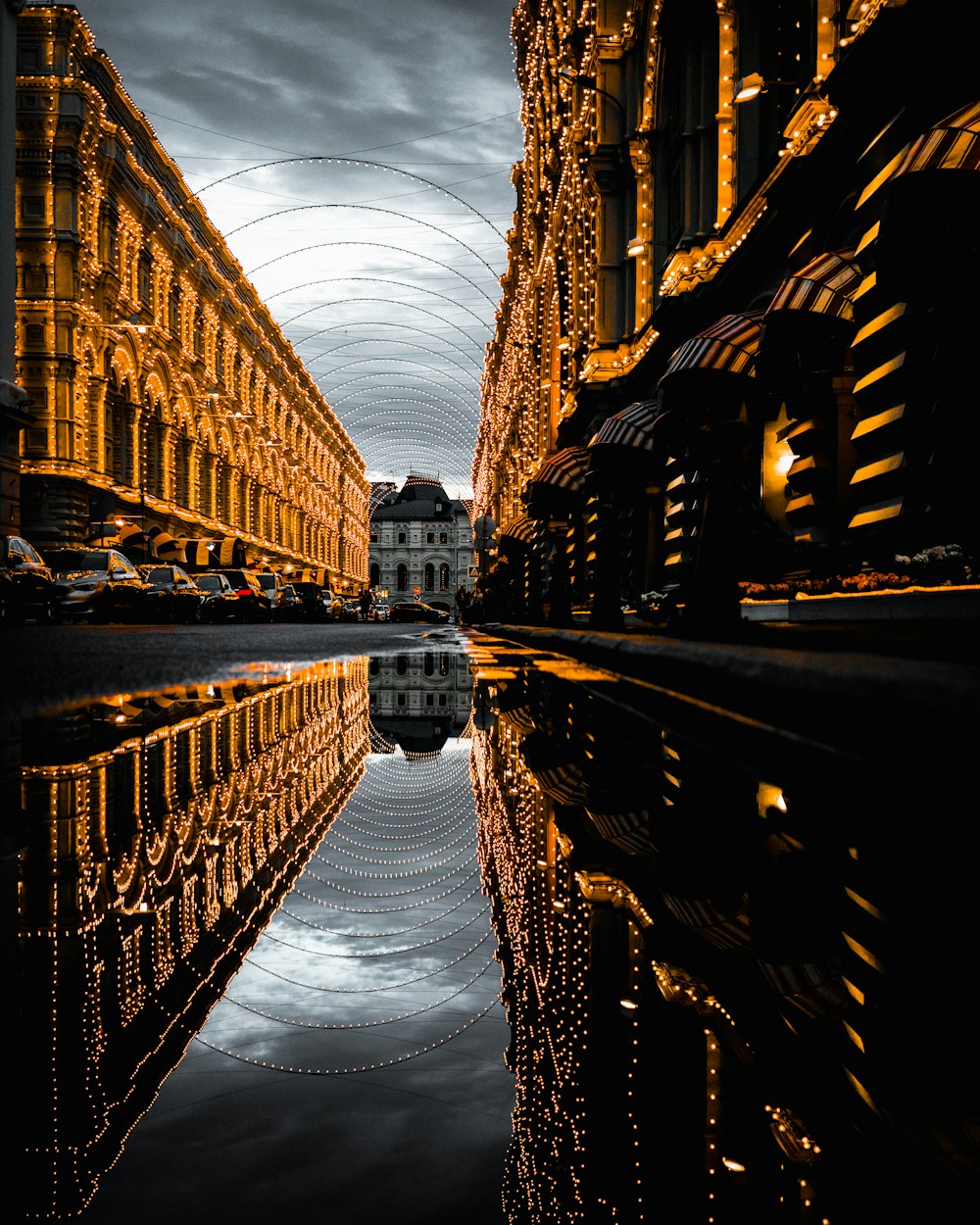 water on asphalt road with reflection of fully-decorated buildings under cloudy sky