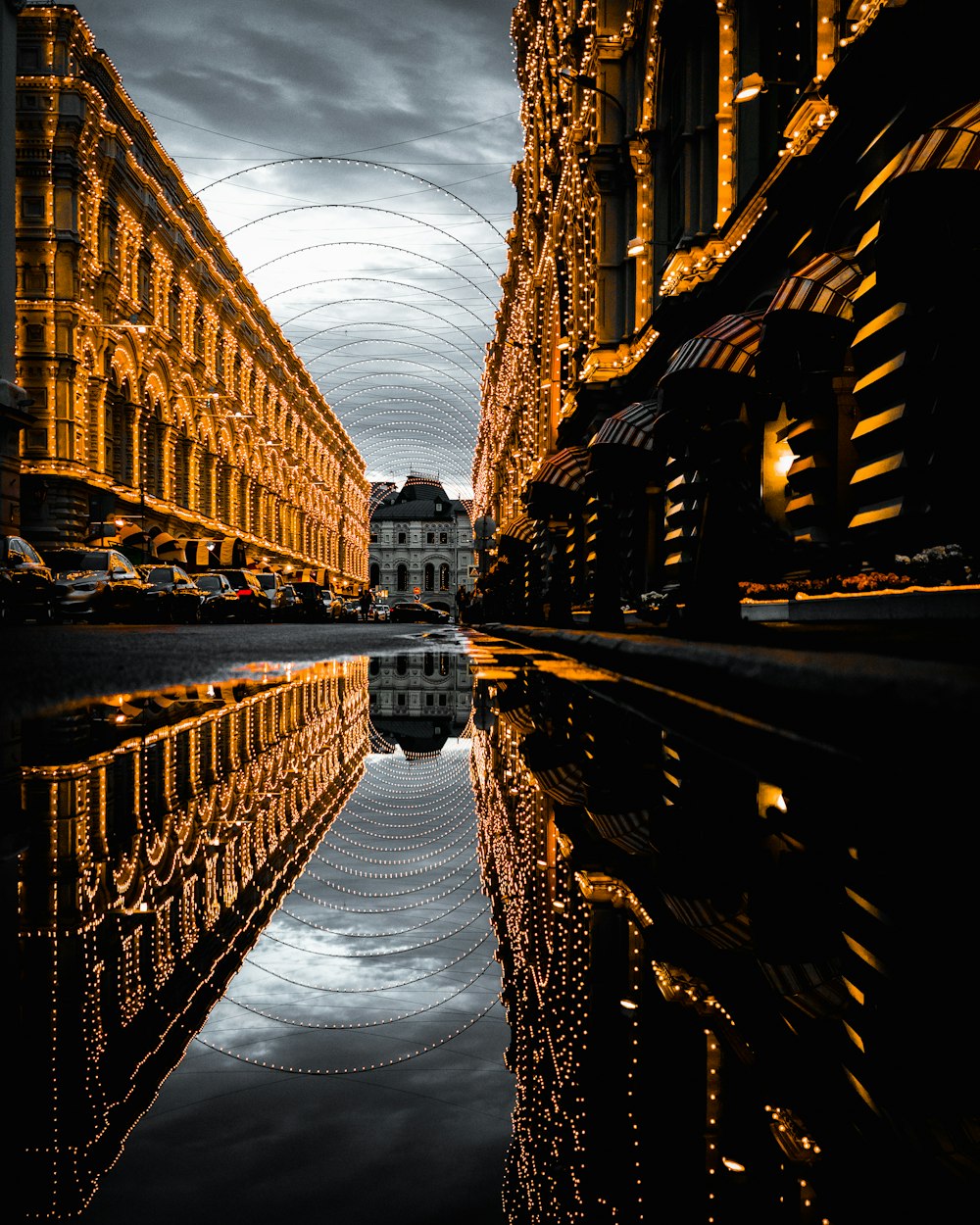 De l’eau sur une route goudronnée avec le reflet de bâtiments entièrement décorés sous un ciel nuageux