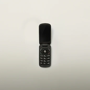 A compact flip phone open to reveal its keypad, sitting on a wooden table with soft lighting.