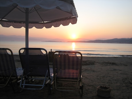 A serene beach at sunset with a comfortable lounge chair and a suitcase nearby, symbolizing a perfect vacation.