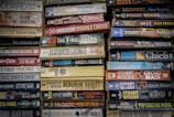 Stacks of paperback books arranged closely together, with a variety of titles and authors visible on the spines. The colors of the book covers range from muted tones to bright hues, creating a mosaic of literary works.