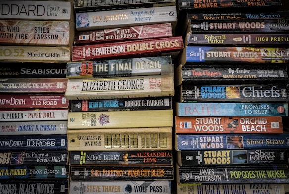 Stacks of paperback books arranged closely together, with a variety of titles and authors visible on the spines. The colors of the book covers range from muted tones to bright hues, creating a mosaic of literary works.