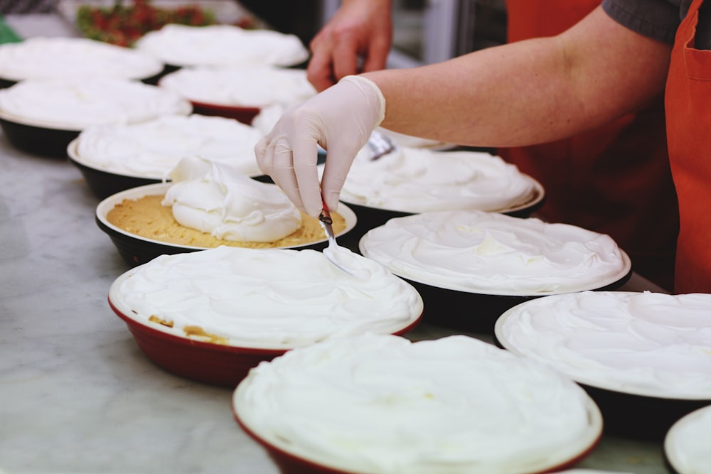person wearing white latex gloves putting cream on bowls