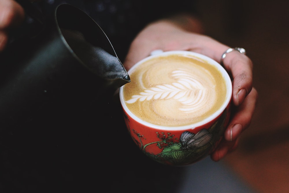 person doing coffee art on red ceramic mug