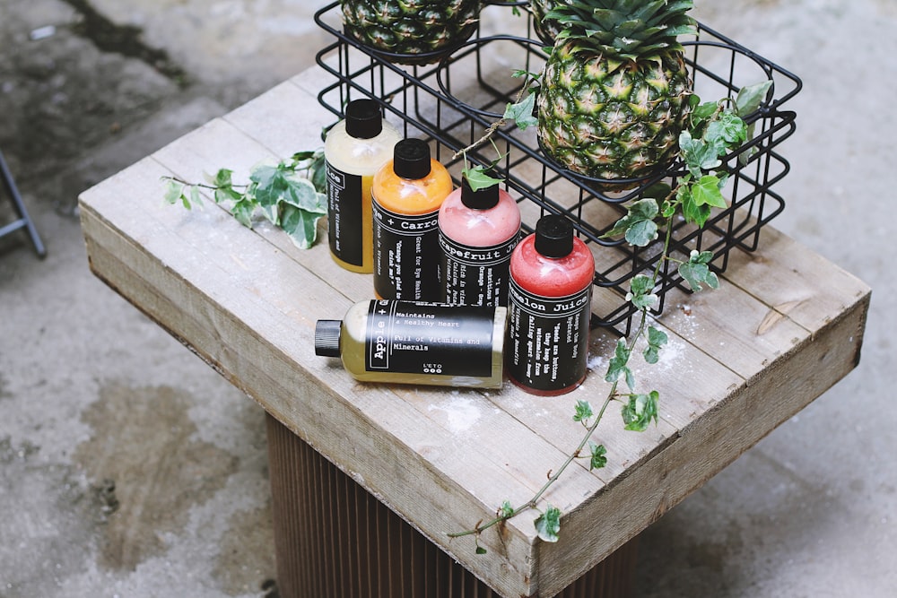 five assorted bottles on brown table beside two pineapples