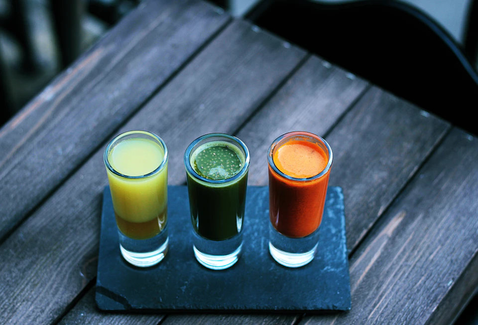 Tiga gelas kecil jamu kuning, hijau, dan merah
