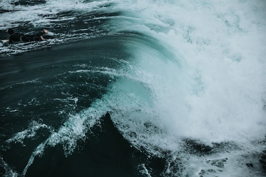 A powerful wave crashing in the ocean, with a surfer riding the wave near the crest. The water appears turbulent with white foam and splashes, adding to the dynamic movement captured in the scene.