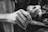 A close-up black-and-white image of a person's hands engaged in a detailed activity. One hand holds a small, pointed tool, while the other hand supports the task being performed. The focus is on the textures and movements of the hands, emphasizing precision and concentration.