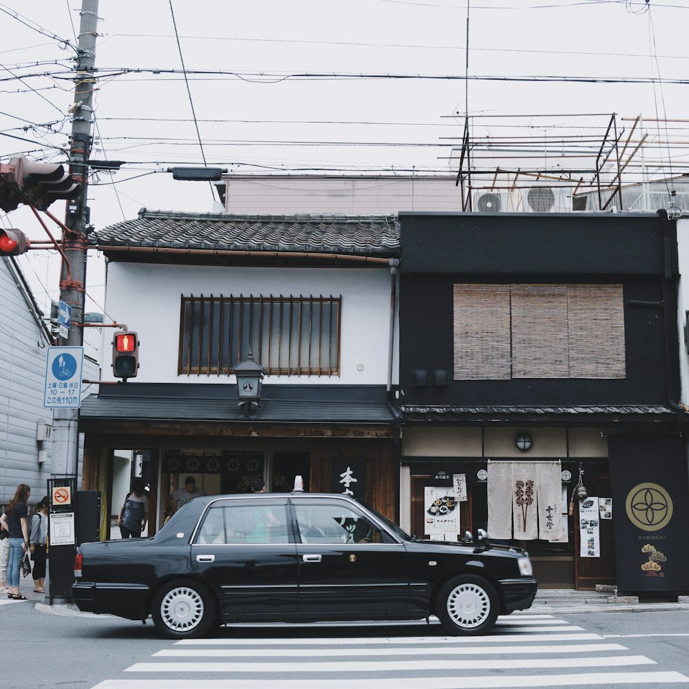 black sedan in front of black and white 2-storey house