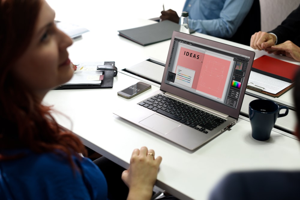 A woman sitting at a laptop with an “Ideas” slide on its screen in a conference room