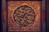 Ornate wooden carving featuring an intricate design of dragons amidst swirling clouds, showcasing exceptional craftsmanship with detailed textures. The deep brown hues of the wood are complemented by the play of shadows in the carving's recesses.