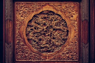 Ornate wooden carving featuring an intricate design of dragons amidst swirling clouds, showcasing exceptional craftsmanship with detailed textures. The deep brown hues of the wood are complemented by the play of shadows in the carving's recesses.